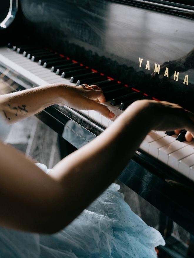 A close view of hands playing the upper keys of a Yamaha grand piano