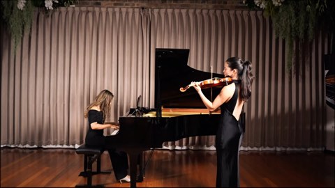 A violinist and pianist performing before a draped backdrop