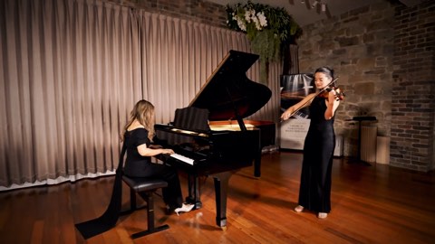 A pianist at a grand piano with a violinist standing alongside