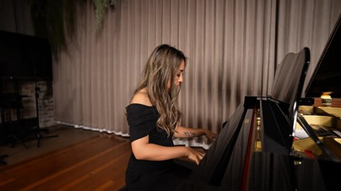 Adlina at a grand piano before a draped backdrop with greenery