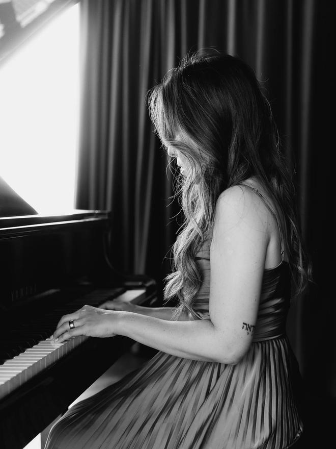 Adlina playing piano in profile with her hands on the keys, in black and white