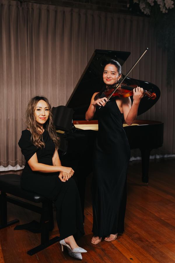 A violinist and a pianist beside a grand piano, both dressed in black
