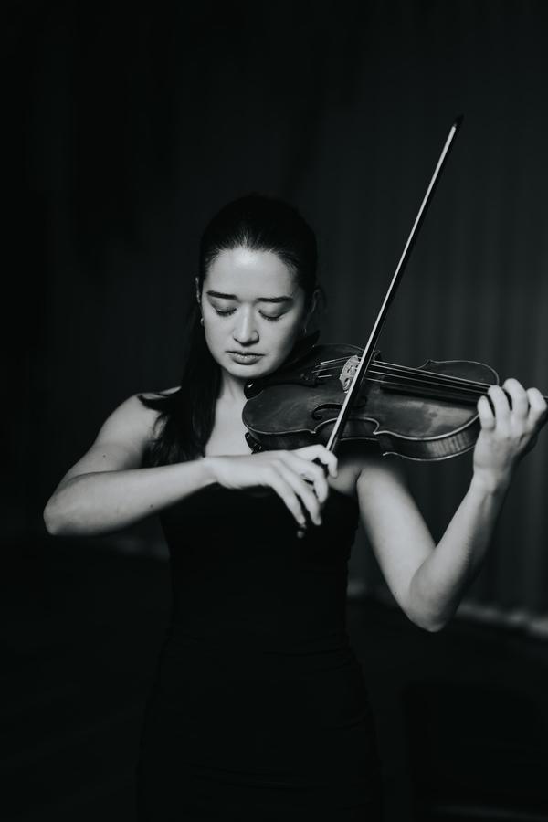 A violinist mid-phrase against a dark background, in black and white