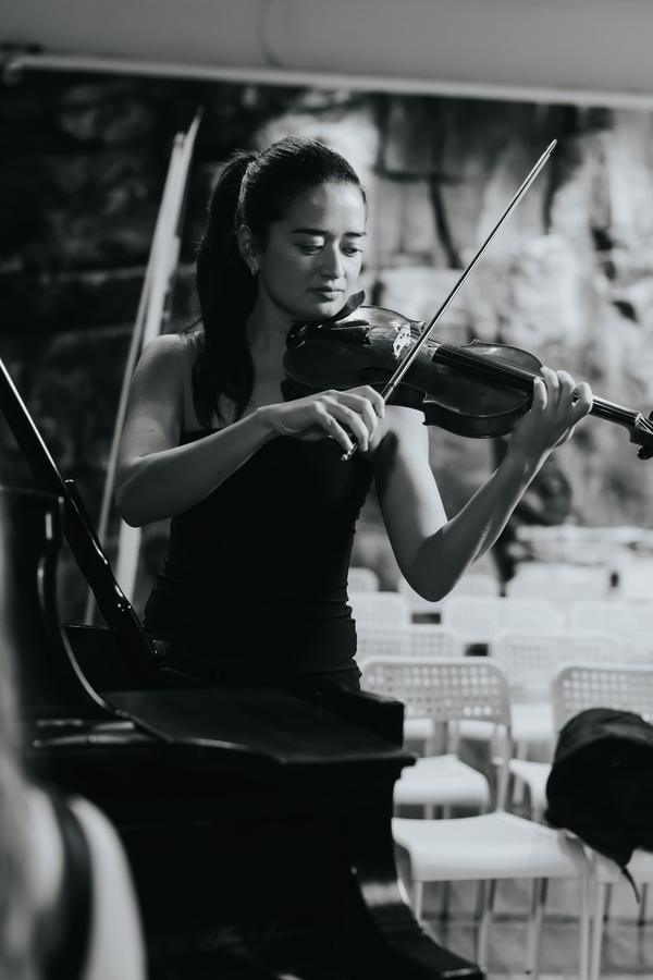 A violinist playing before rows of white ceremony chairs, in black and white