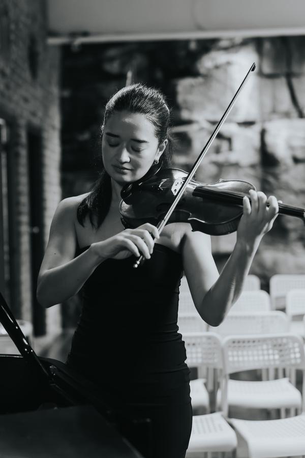 A violinist playing beside a sandstone wall, in black and white